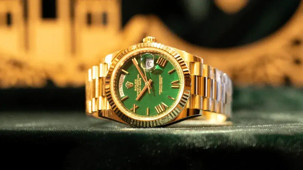 A close - up of a high - end Rolex watch featuring a green dial, gold casing, and gold bracelet, with day and date display.